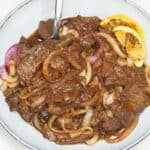 Bistek tagalog filipino steak and onions on a plate with a spoon.