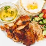 Chicken Tocino (Cured Chicken) with garlic rice topped with egg, vinegar dipping sauce and a salad on a plate.