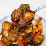 Eggplant stir fry with shrimp on a plate scooped by a spoon.