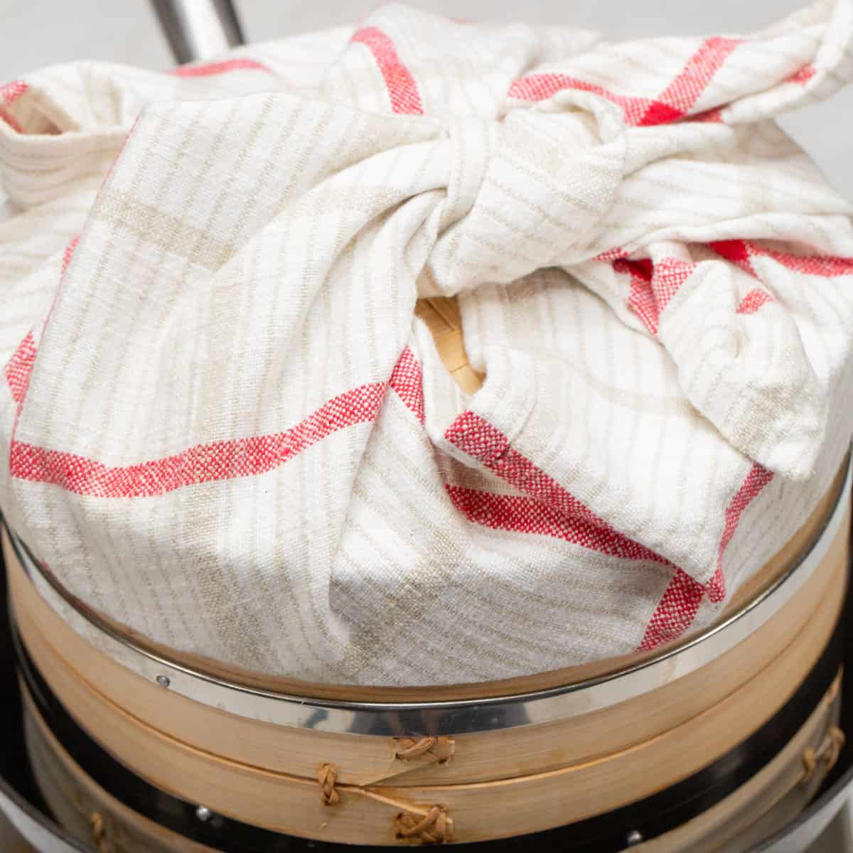 A steamer basket in a wok with the lid covered with a cloth.