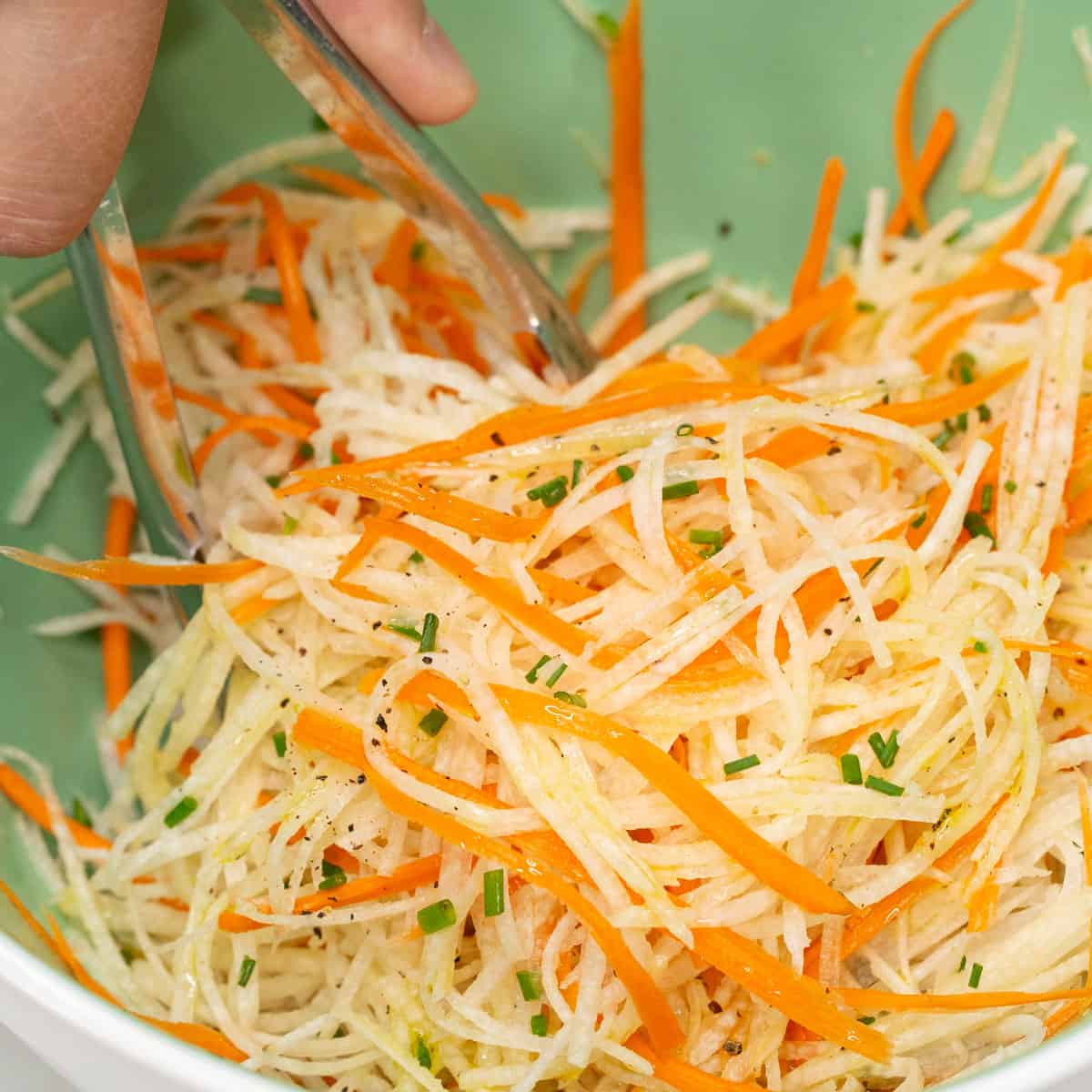 Tossing the salad in the bowl using a pair of tongs.