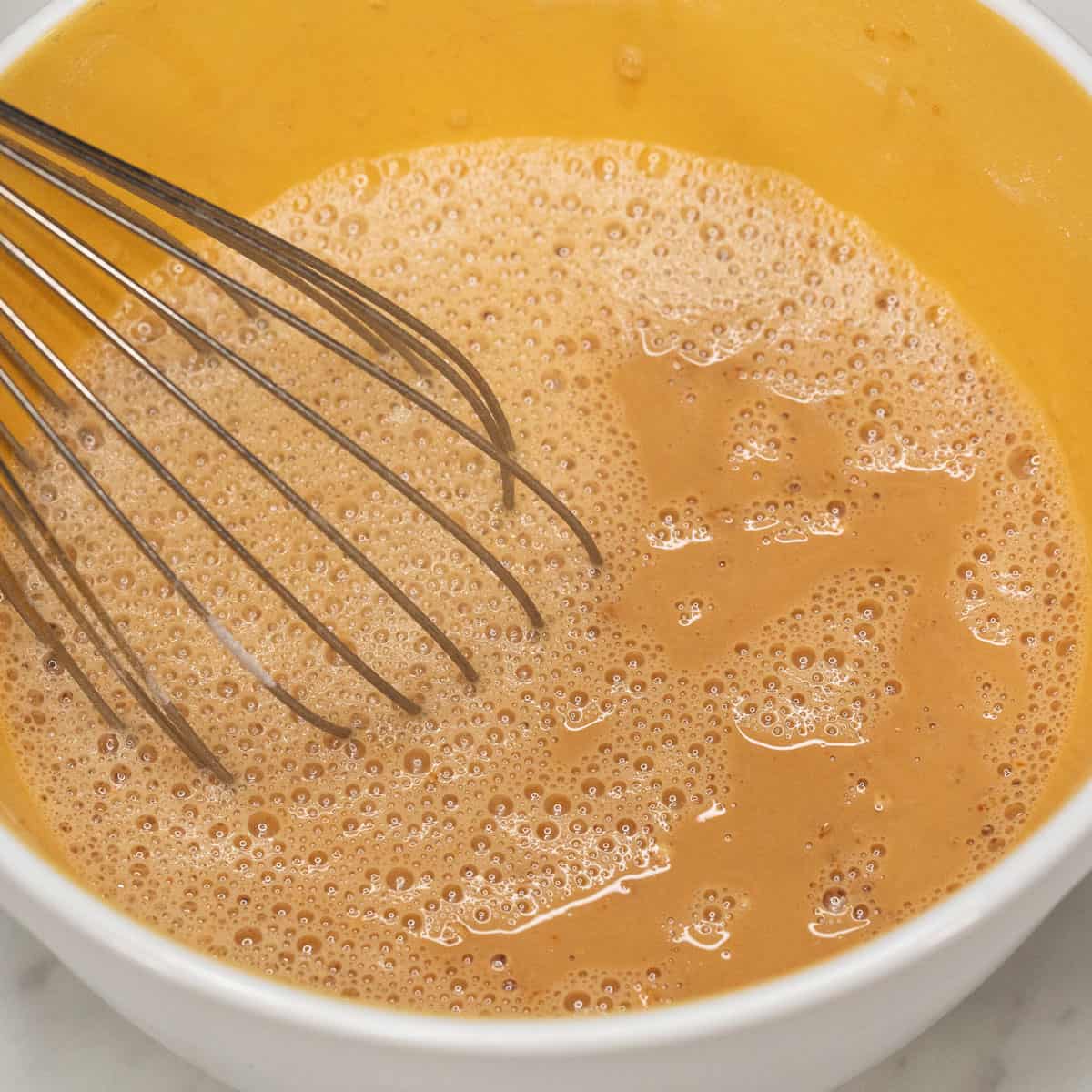 Mixing the ingredients for kutsinta using a whisk.