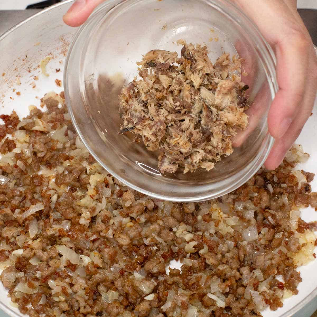 Adding tinapa flakes to the pork and aromatics in the pan.