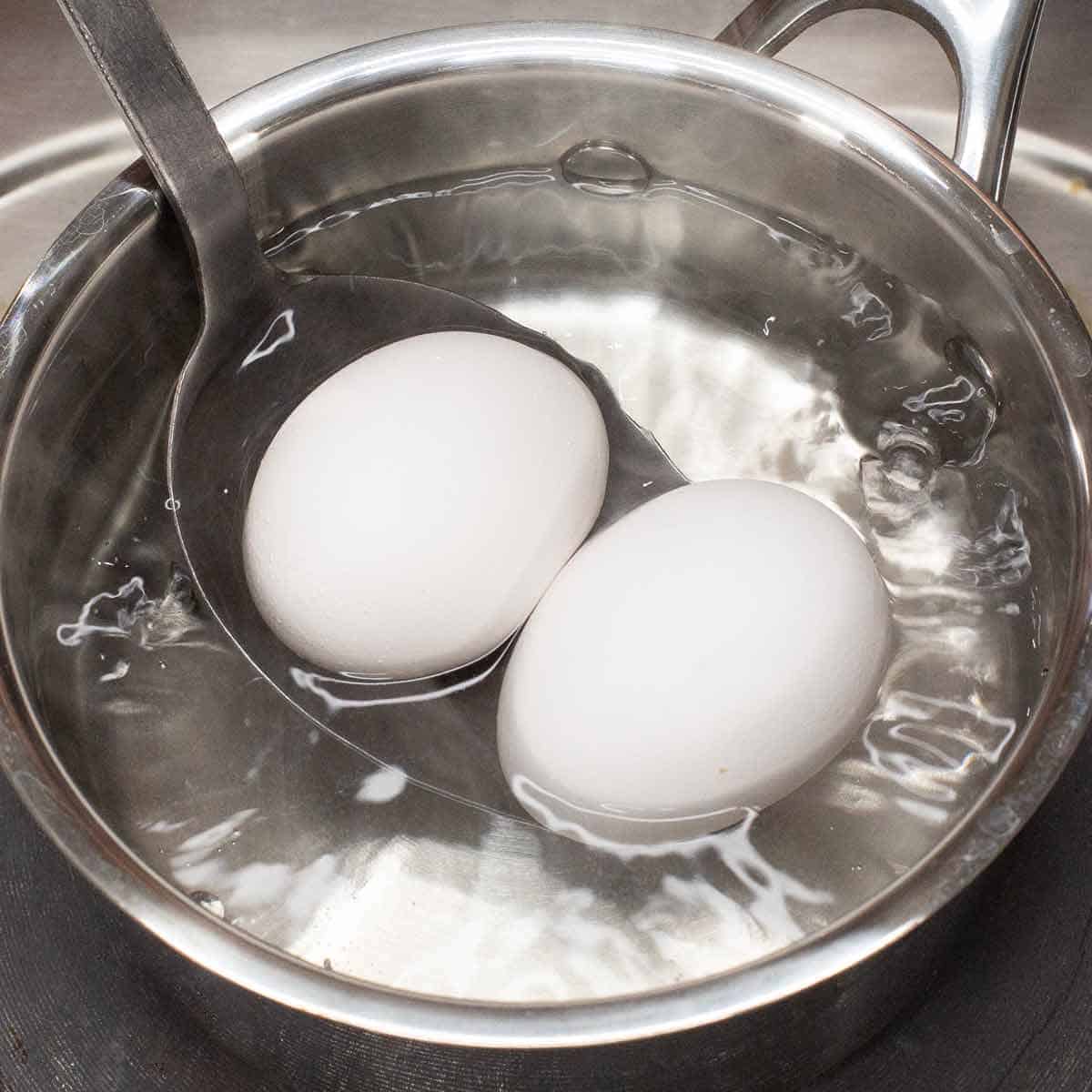 Gently dropping the eggs in the boiling water using a ladle.