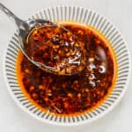 Chilli Garlic Oil in a bowl scooped by a spoon.