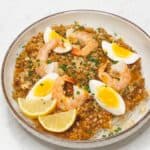 Pancit palabok topped wtih sliced soft boiled egg, shrimp, and sliced lemon in a bowl.
