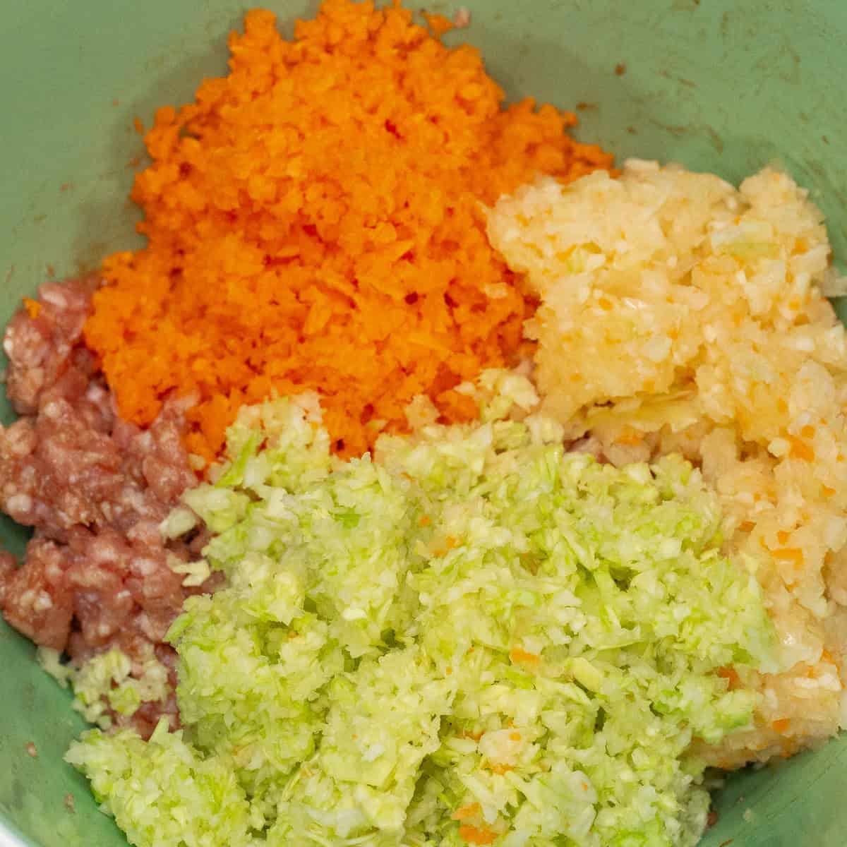 Finely chopped vegetables added to the ground pork mixture in the bowl.