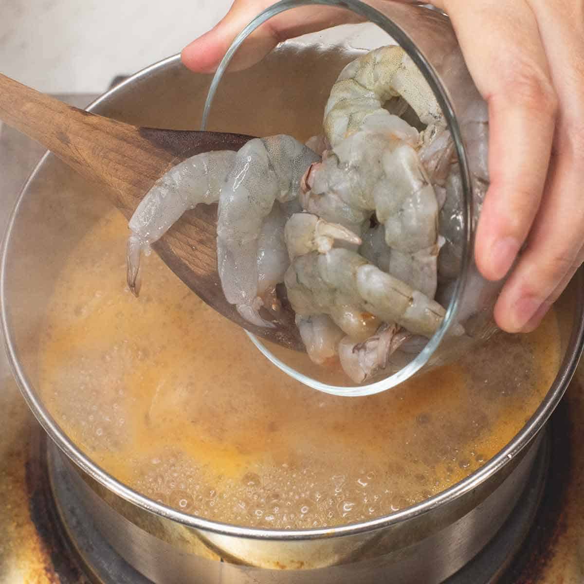 Adding the raw shrimp to the boiling liquid to poach them.