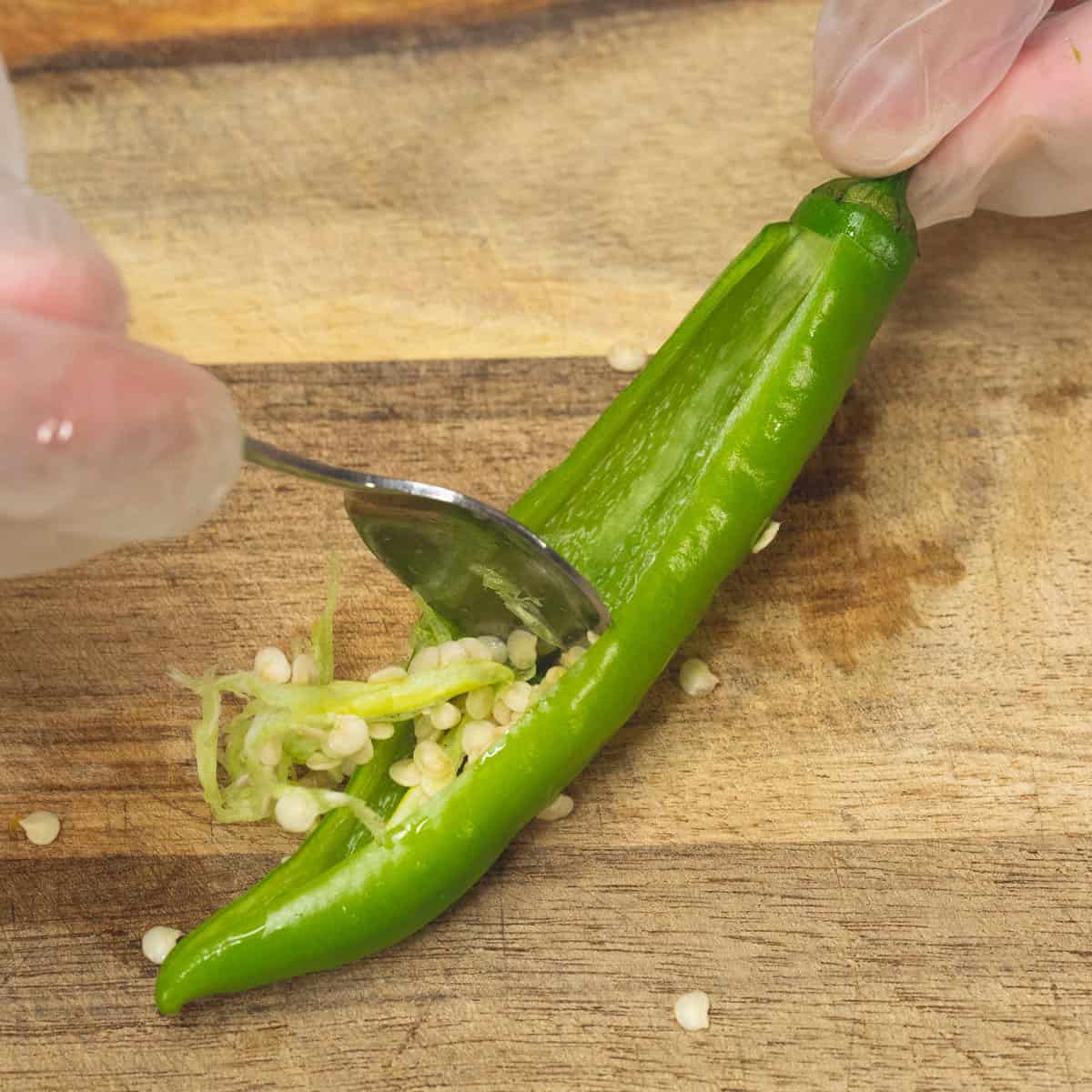 Cutting an opening in the chili peppers and scraping the seeds out with a spoon.