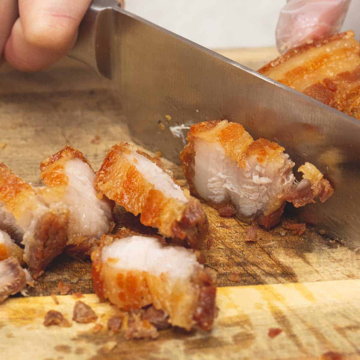 cutting the fried pork belly into thin bite-sized pieces.