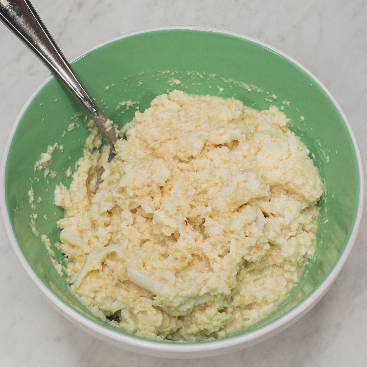 Mixing grated cassava, sugar, and coconut milk in a bowl.