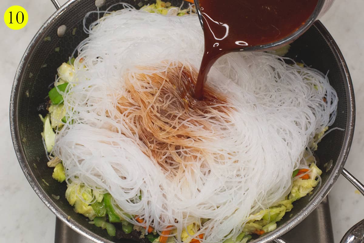 Pouring the liquid mixture over the noodles in the wok.