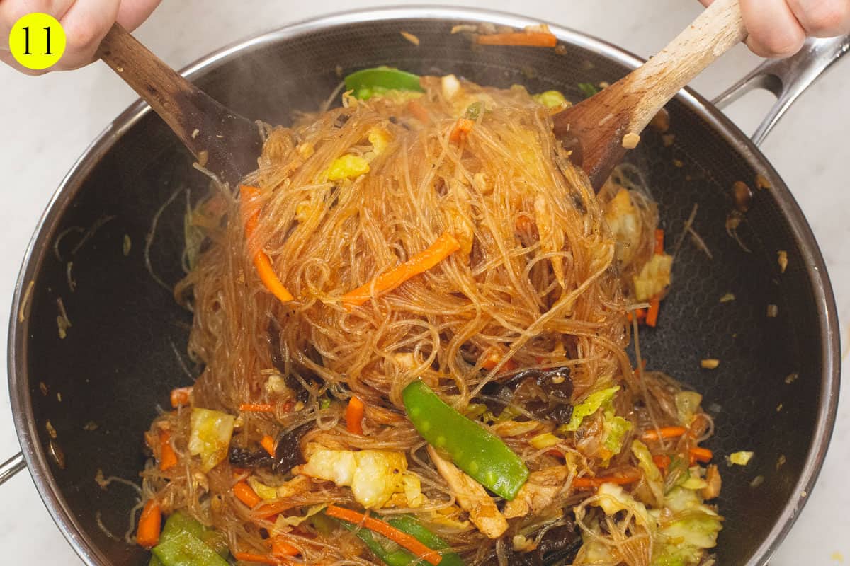Tossing the Sotanghon Guisado in the wok using two wooden spoons.
