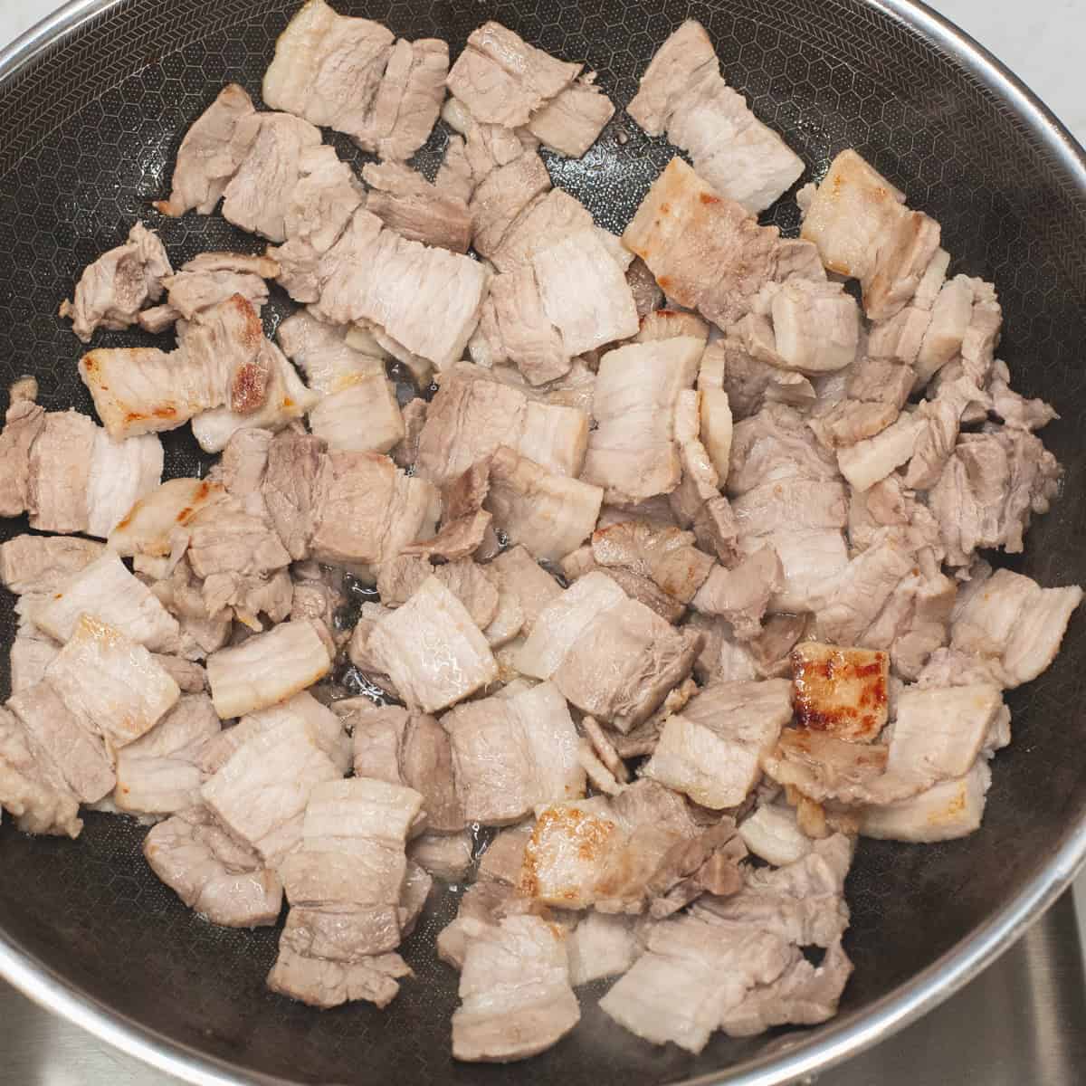 Browning the pork belly slices in a wok.
