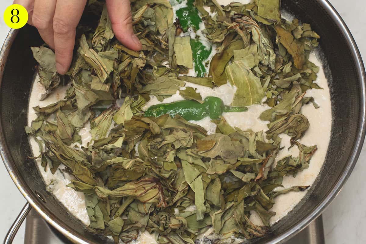 Submerging the dried taro leaves in the coconut milk mixture.