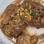 Burger Steak topped on a rice on a plate.