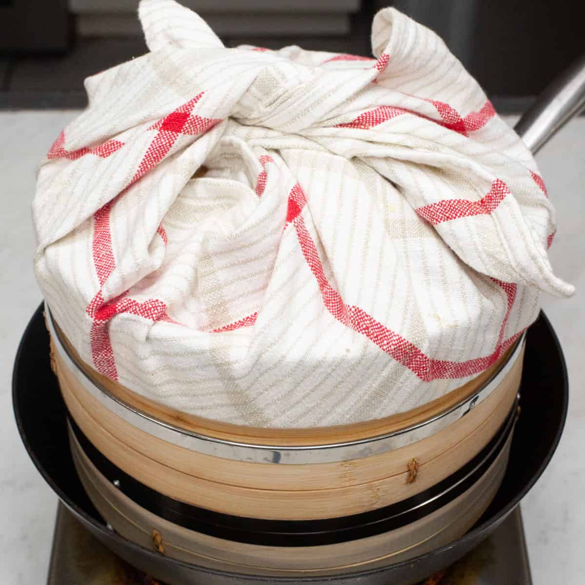 Steaming the puto in a wok with the lid wrapped with towel.
