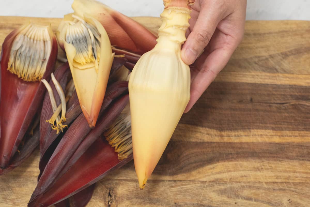 Holding the core of the banana blossom with the purple layers on a cutting board.