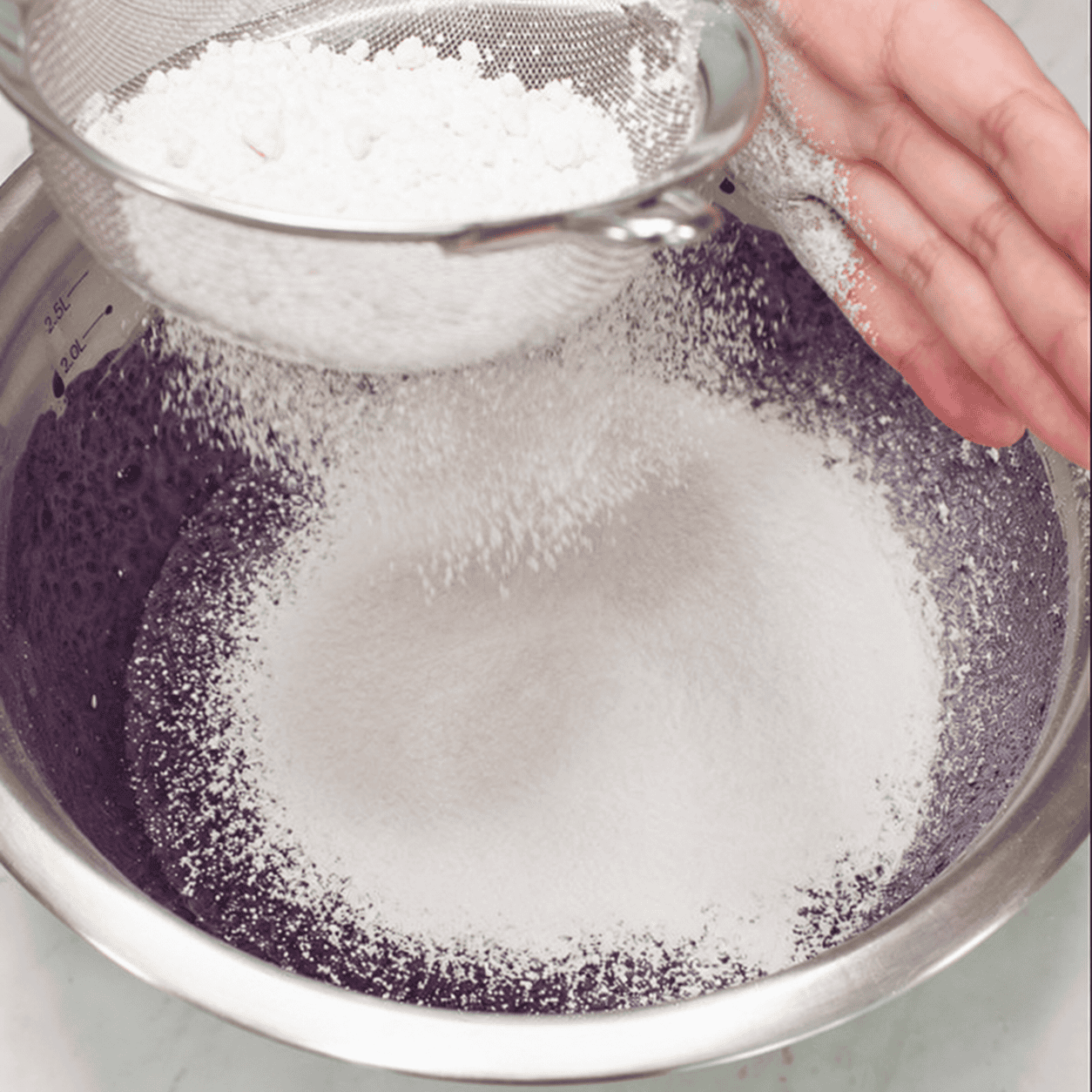 Sifting dry ingredients into the ube batter.