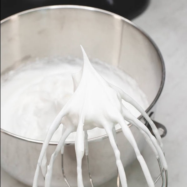 Whipped meringue holding a firm peak on the whisk.