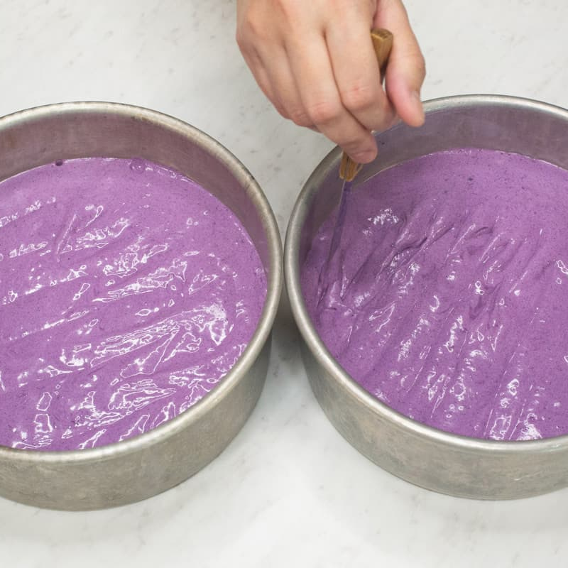 Running a knife through the ube cake batter in a round pan.