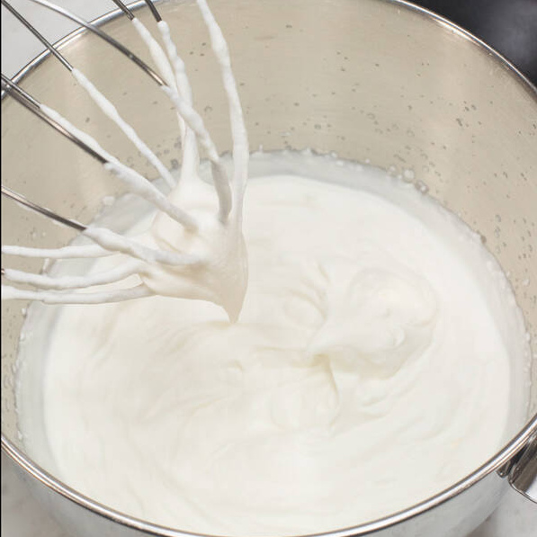 Whipped cream frosting holding a firm peak on the whisk.