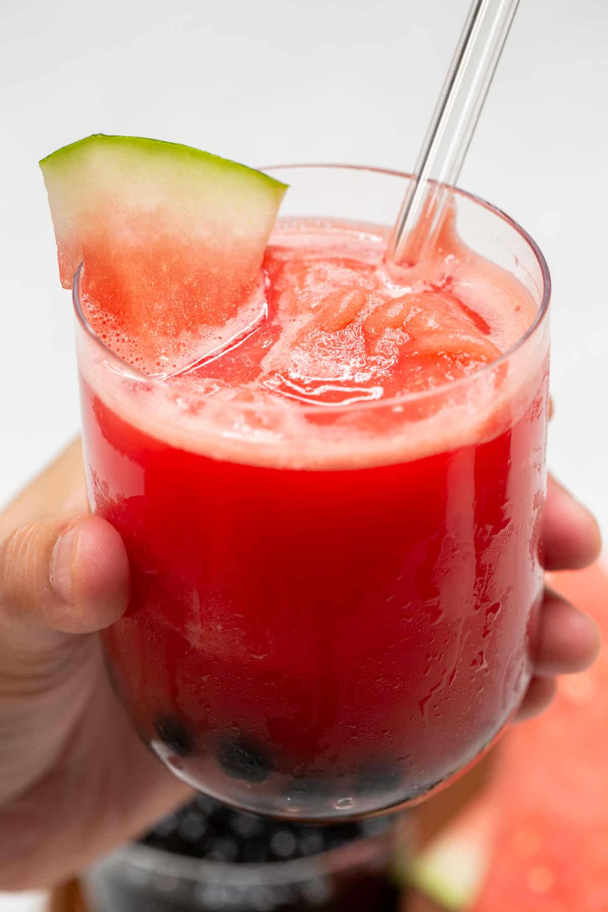 Holding a glass of watermelon slushie with boba.
