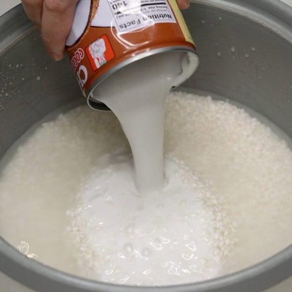 Adding coconut milk to glutinous rice in the rice cooker.