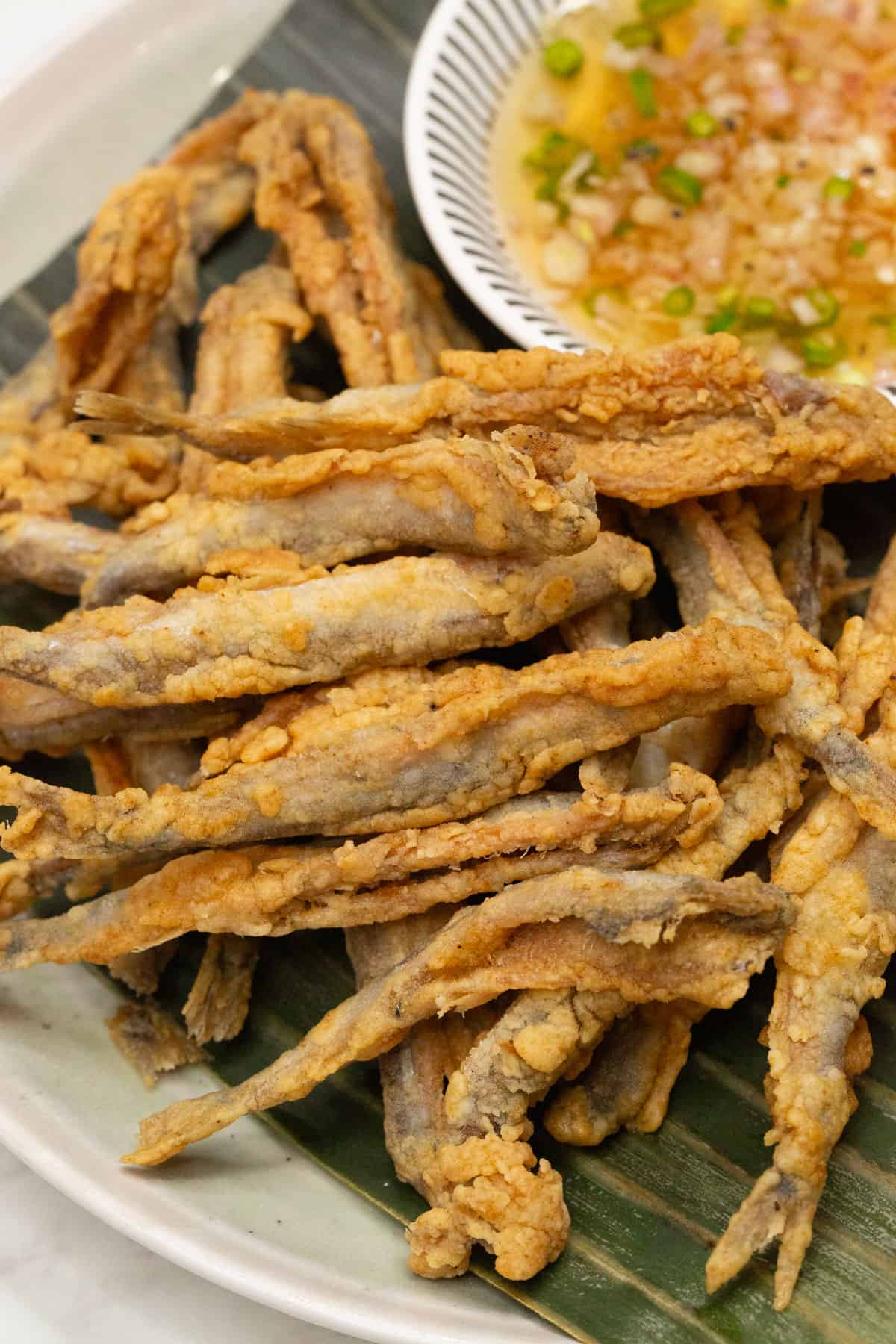 Crispy fried smelt on a banana leaf-lined platter, served with dipping sauce on the side.