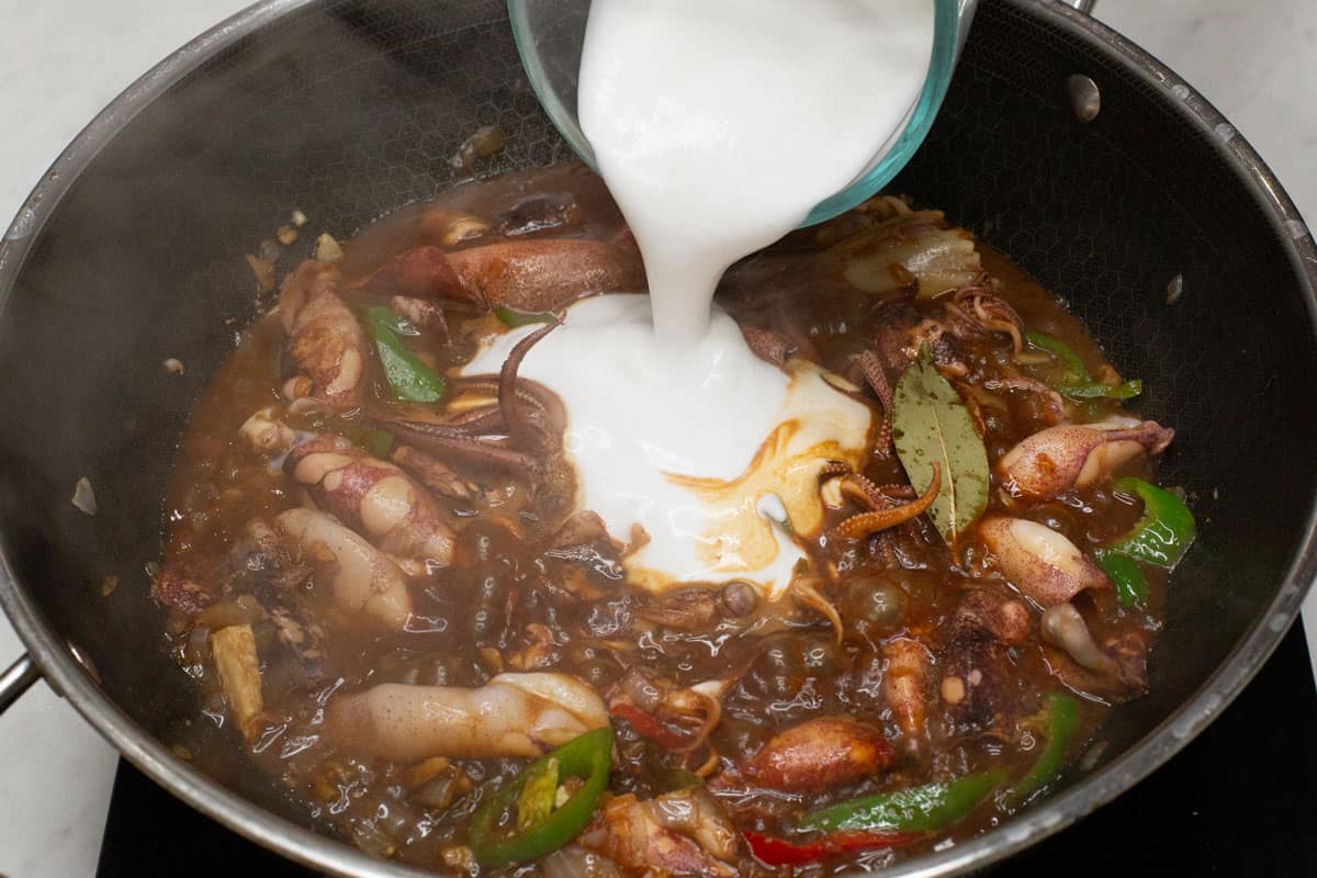 Adding coconut milk to the squid mixture in a wok.