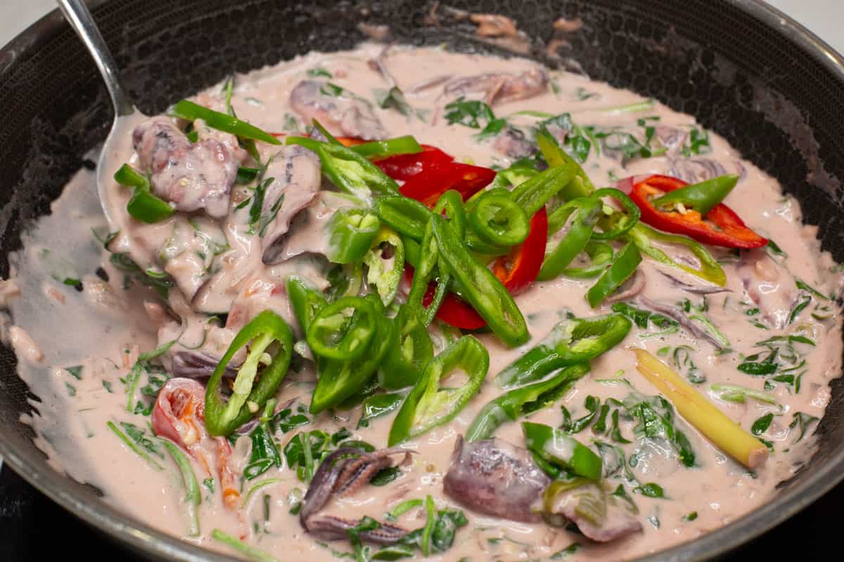 Red and green chilies added to the Ginataang Pusit with Malunggay in a wok.