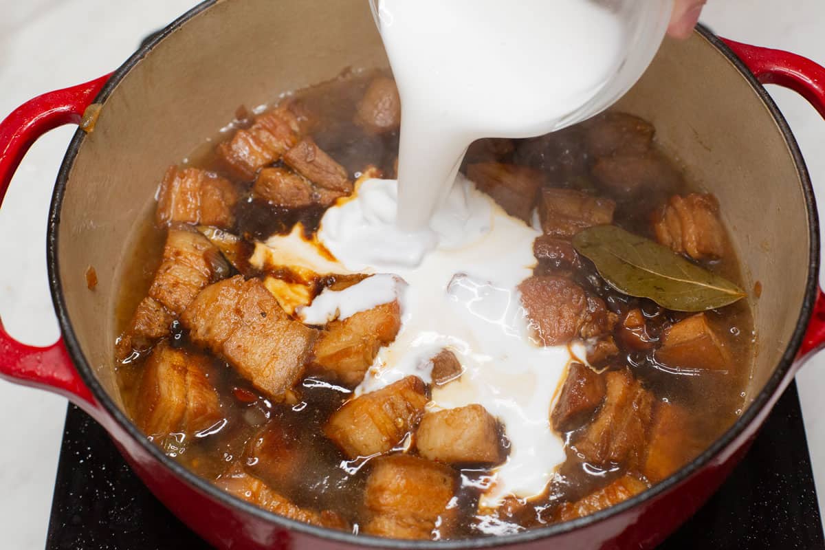 Adding coconut milk to the meat mixture in the pot.