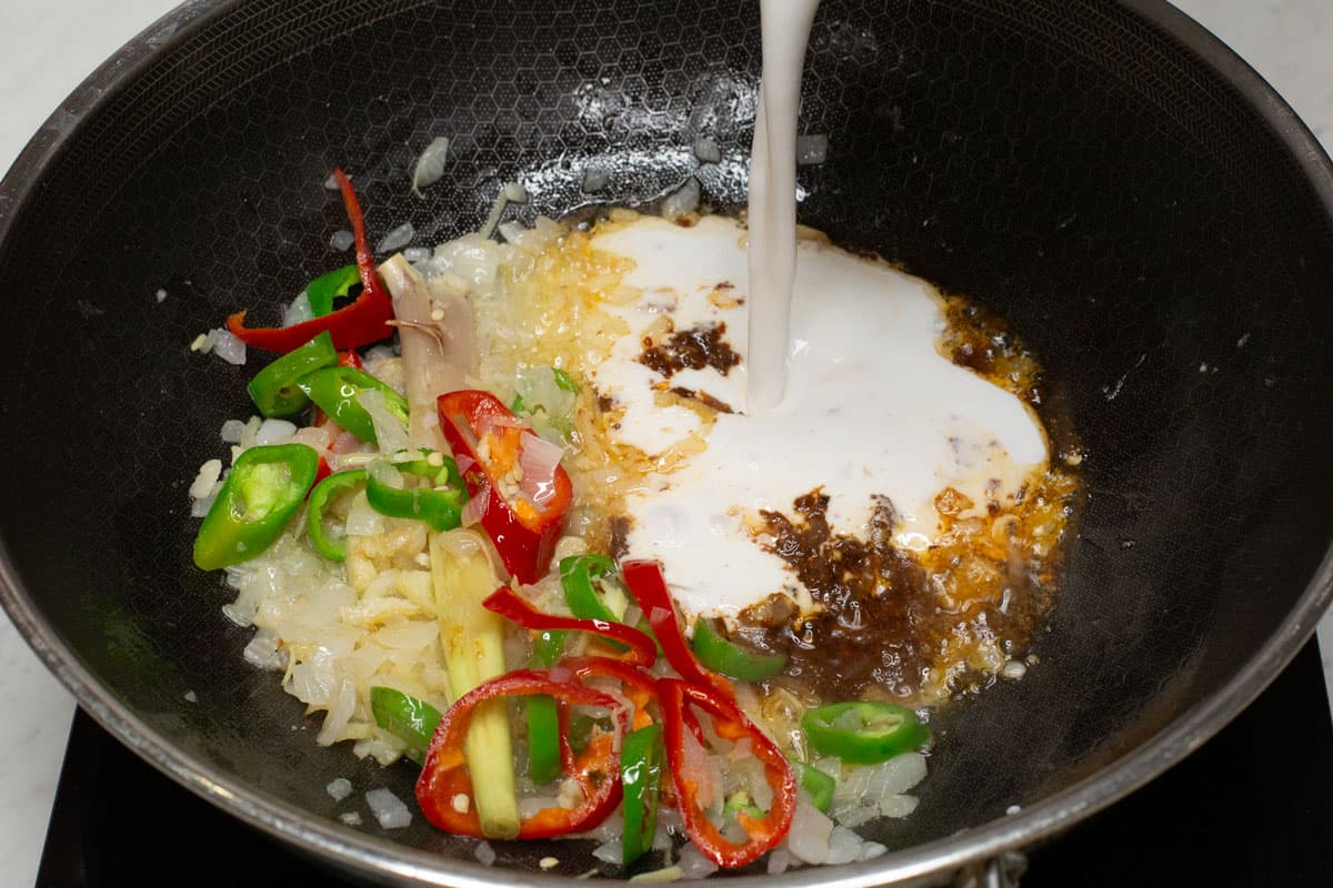 Adding coconut milk to the aromatics and shrimp paste in a wok.