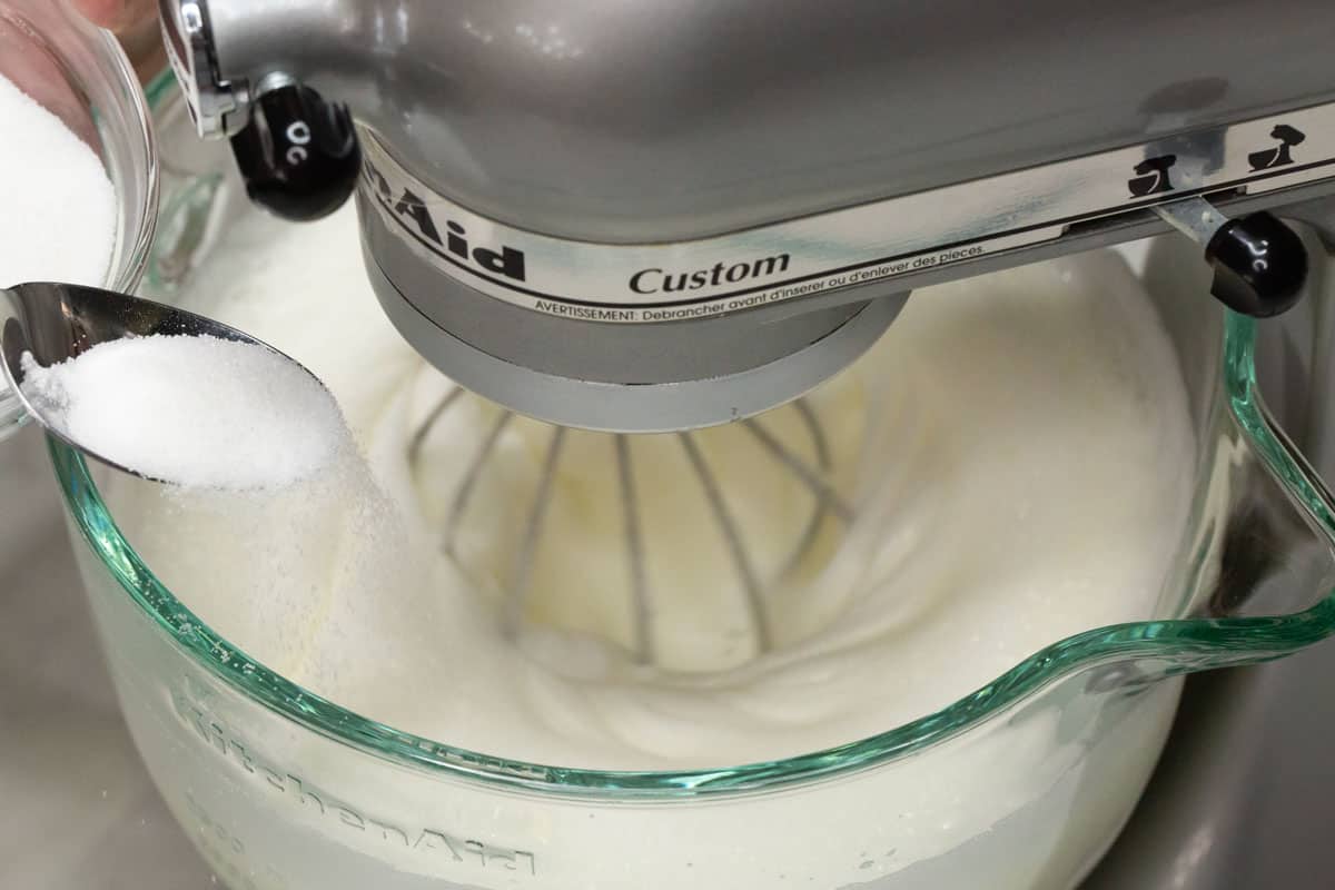 Slowly adding the sugar to the meringue in the bowl.