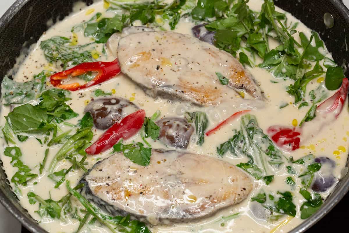 adding fish and greens into the coconut milk