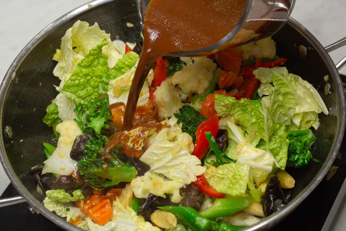 Adding the prepared sauce into the vegetables in the wok.