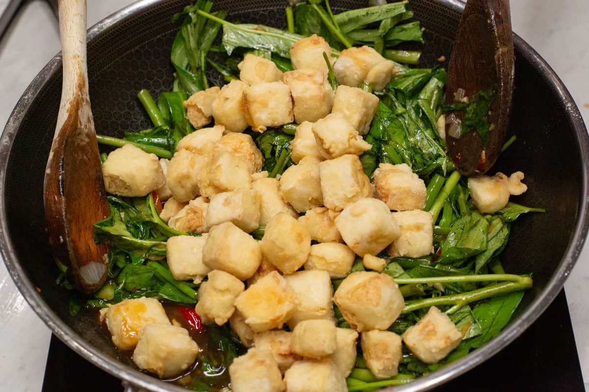 Fried tofu pieces and kangkong in a wok.