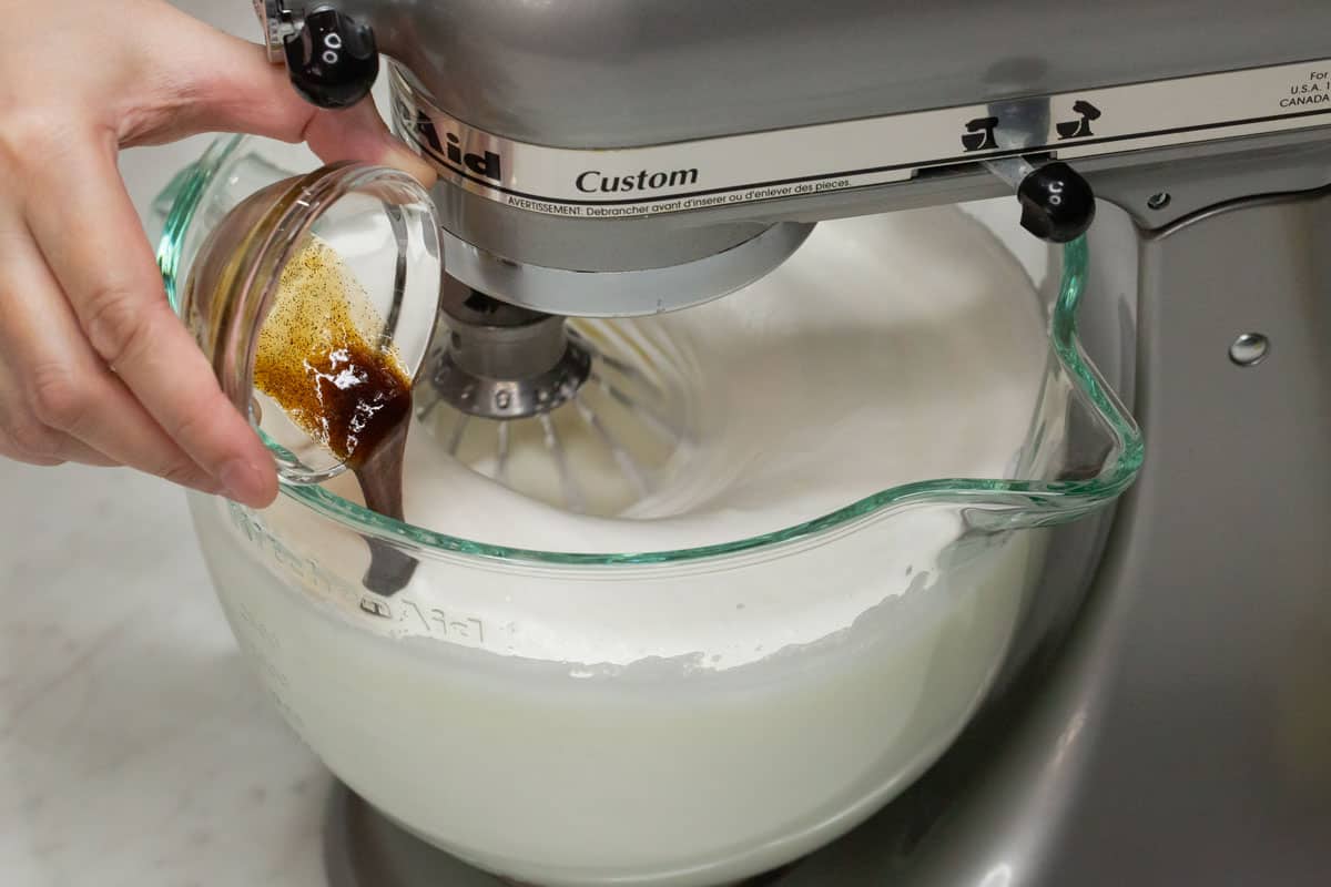 Adding the vanilla paste to the meringue in the bowl.