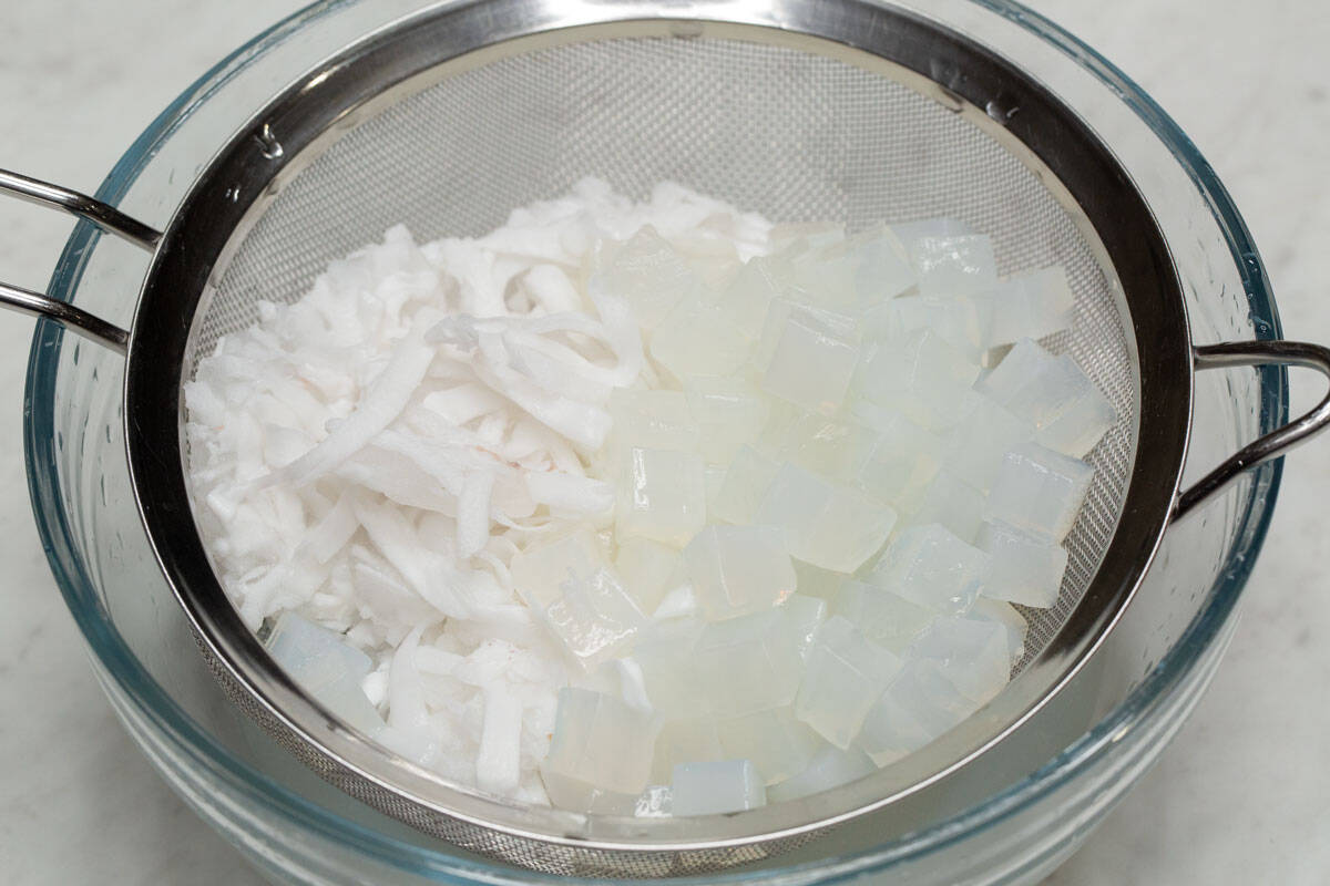 Buko (young coconut strips) and nata de coco in a strainer over a bowl.