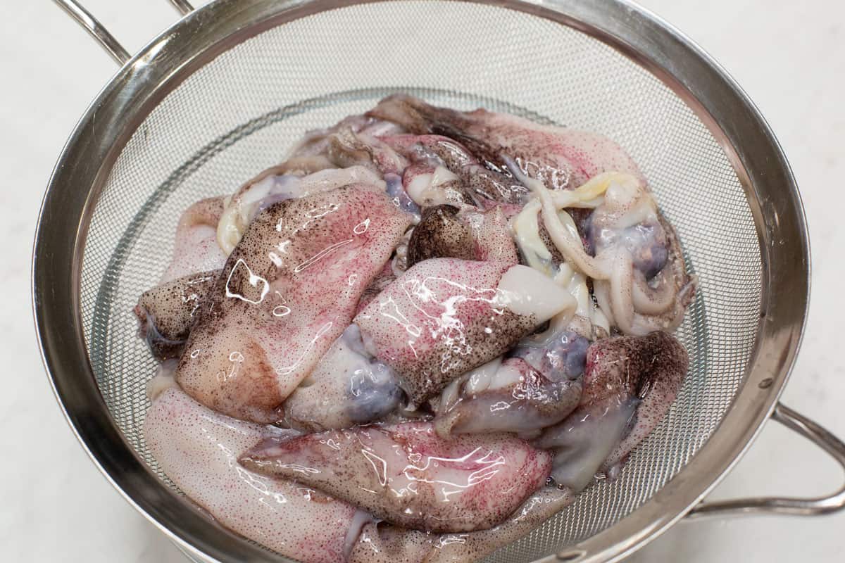 Cleaned squid in a strainer over a bowl.