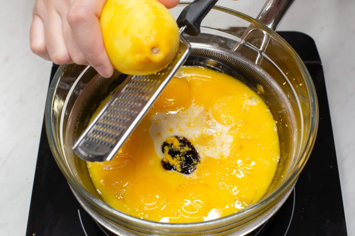 Zesting a lemon directly over a bowl of egg yolk mixture set on top of a pot.
