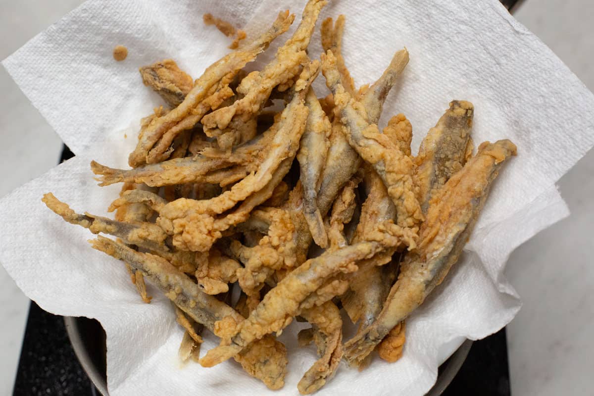 Crispy fried smelt on a paper towel-lined plate.