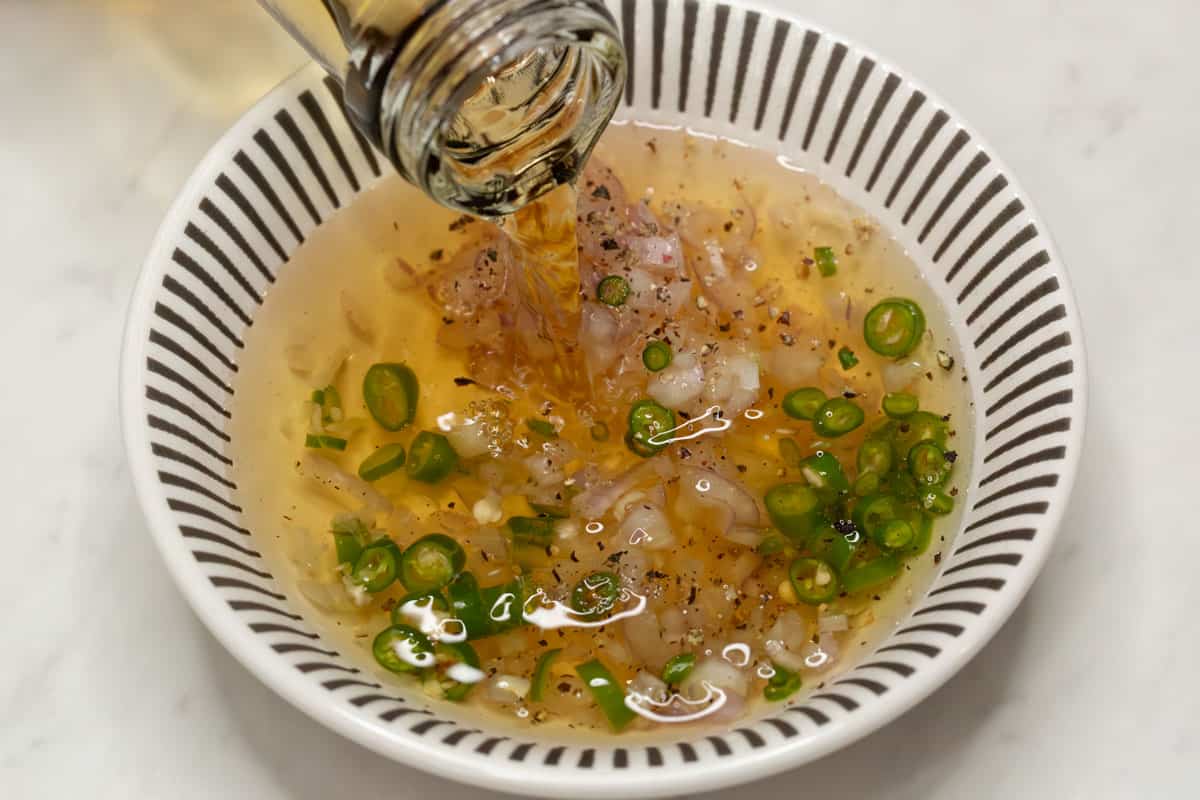 Pouring vinegar to the shallots and chilies in the bowl.