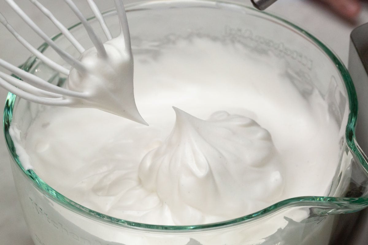 Lifting the whisk to check for stiff peaks.