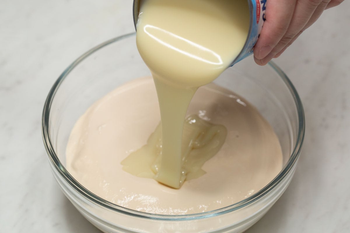 Pouring condensed milk over the cream in the bowl.