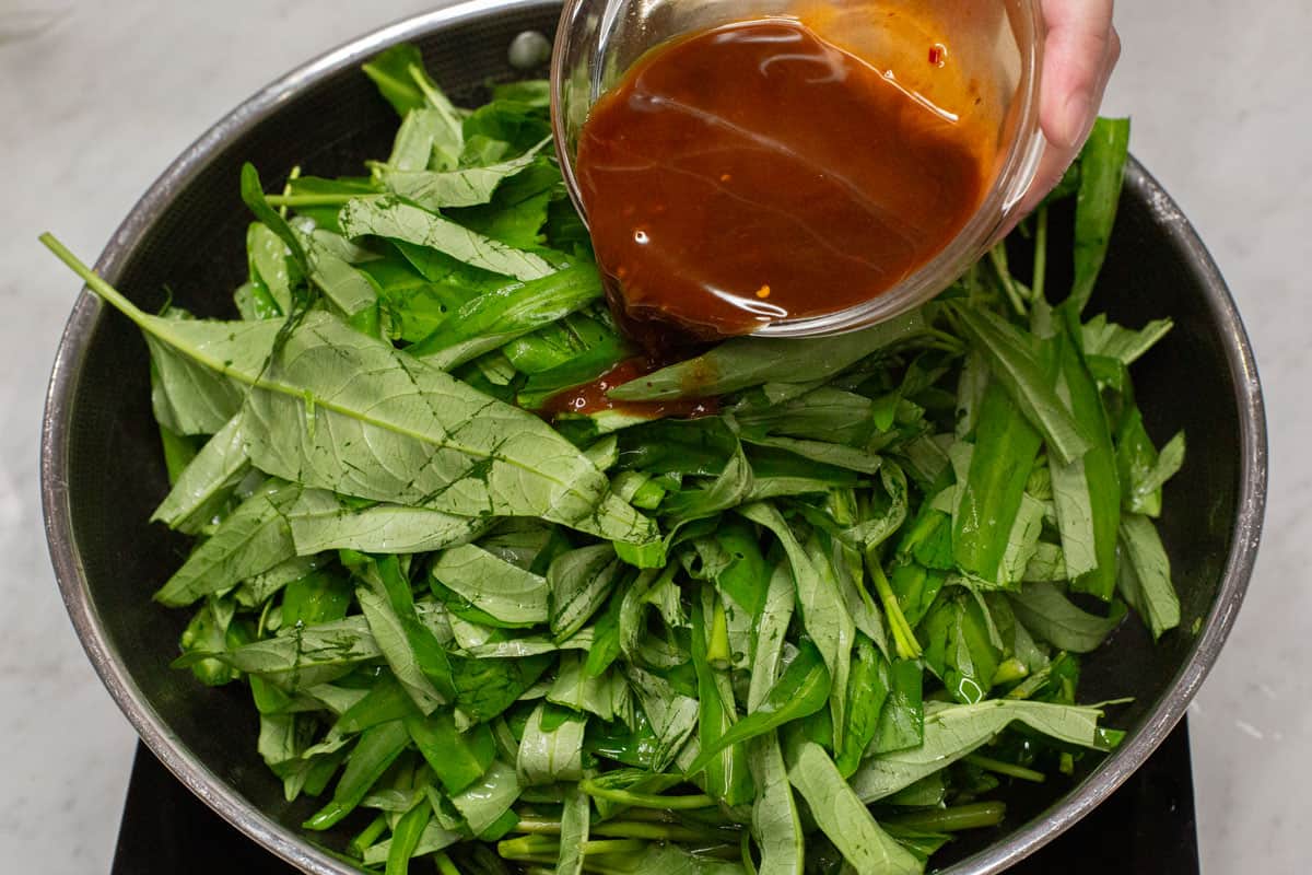 Adding the sauce to the kangkong leaves in a wok.