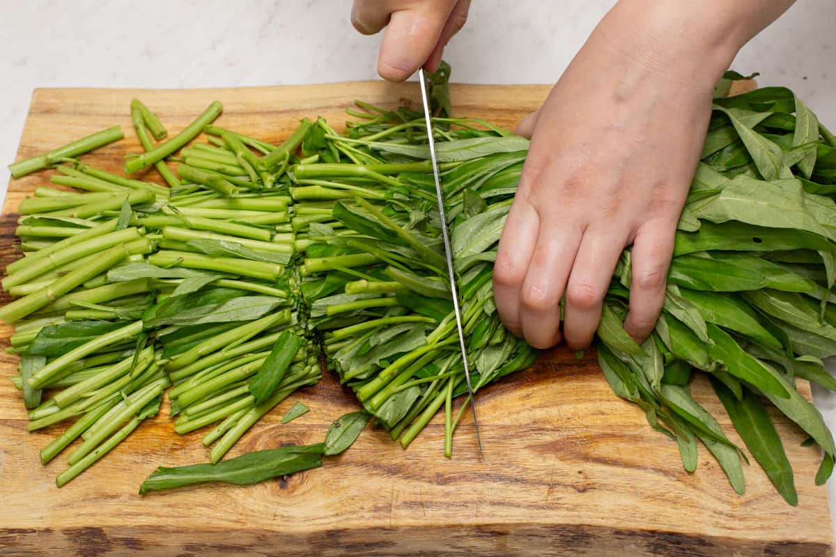 Cutting the kangkong into sections on a cutting board.