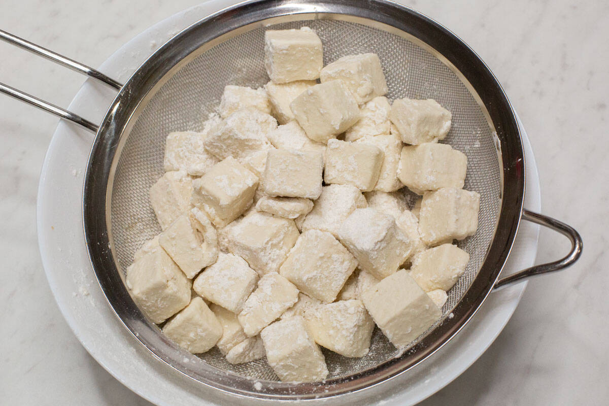 Coated tofu pieces on a strainer over the bowl.