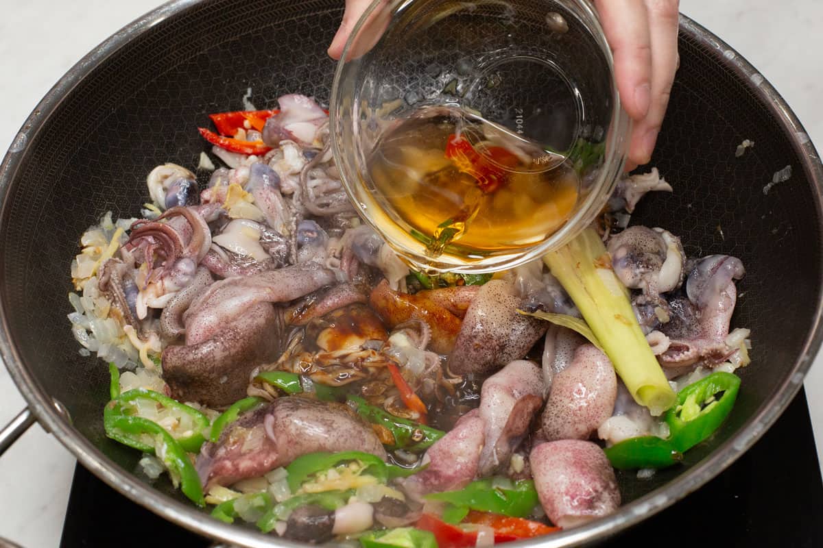 Pouring vinegar to squid and aromatics in a wok.