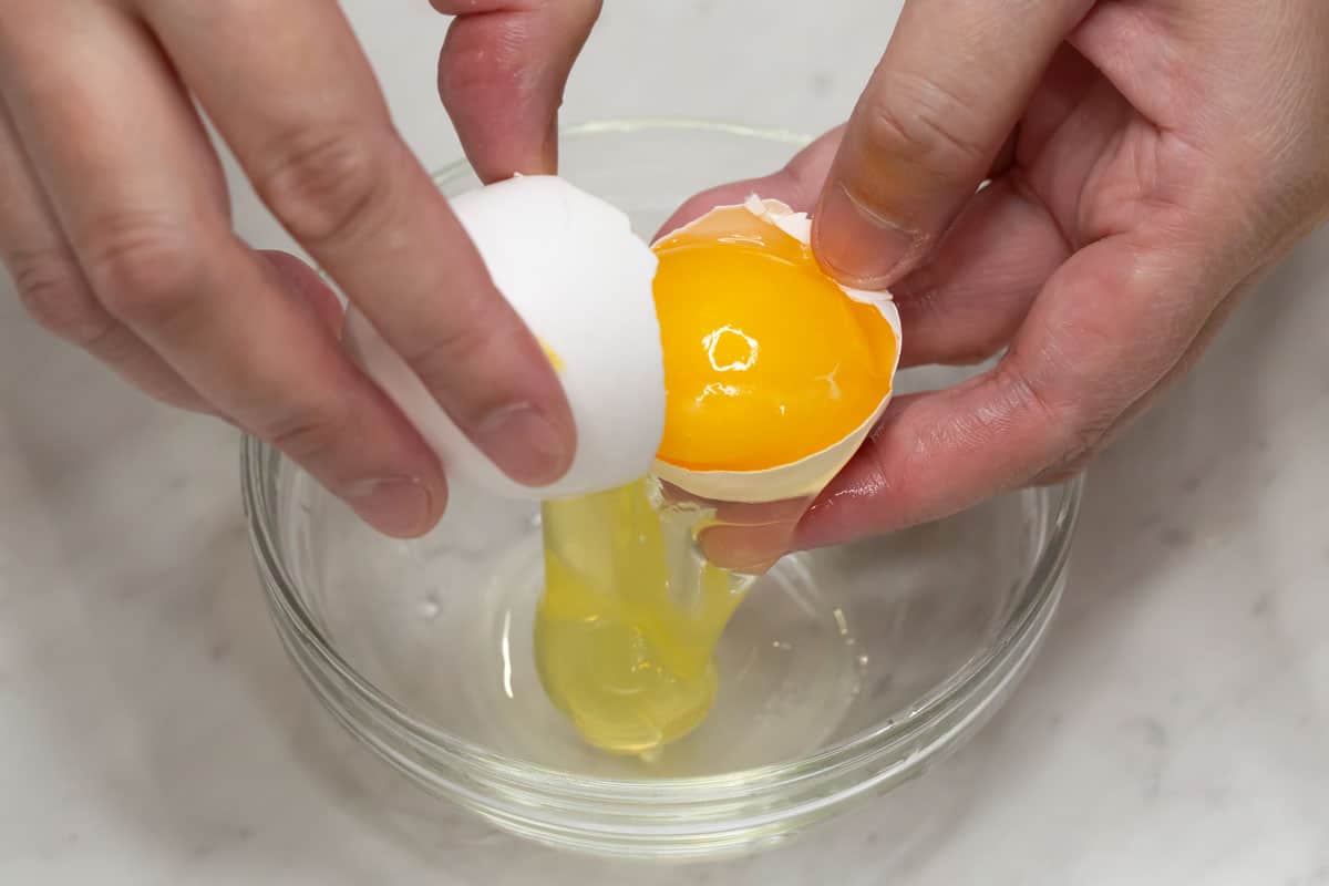 Cracking the egg over a small bowl.